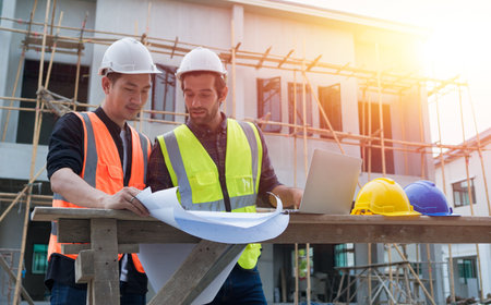 Professional male civil engineers manager or architects and foreman, worker. While meeting discuss inspect with laptop, blueprint building project on construction site. Real estate building concept.の写真素材