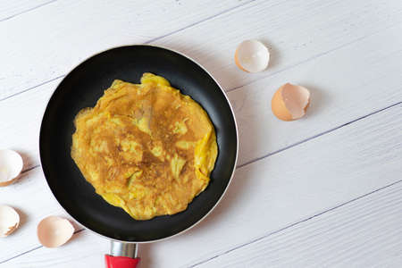 Top view Thai Omelette or fried egg little scorched on black pan. beside egg shell on white table....