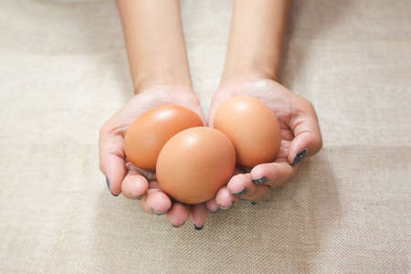 Close up of Young woman hands, holding eggs in the hands on sack background. Care or attentive concept. Selective focus.の写真素材