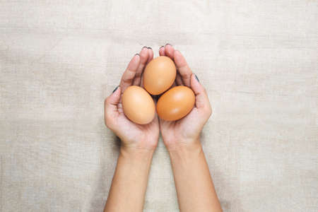 Top view of Young woman's hands, holding eggs in the hands on sack background. Selective focus. Care or attentive concept.の写真素材