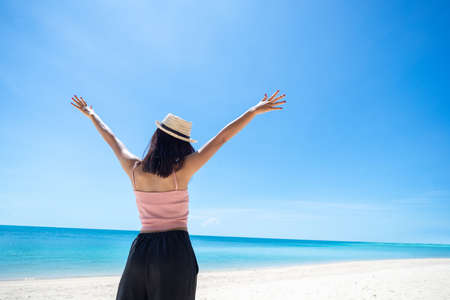 Back of woman tan skin wearing pink tank top and straw hat with standing arms outstretched on sky. looking into the sea and fresh sky. Summer travel. Relax, Holiday and tropical, comfortable concept.の写真素材