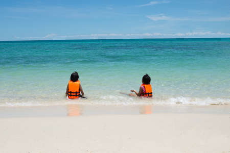 back of asian children girl with life jacket sitting and playing sea water in the sidesea area. Children in nature with beautiful sea, sand and blue sky. summer concept. School Holiday concept.の写真素材