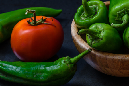 chili pepper and tomato on a dark background. some pepper lie in a wooden bowl. the ingredients for the sauceの写真素材
