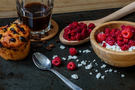 Cottage cheese with raspberries, coffee in a cup and blueberry muffin for breakfast with scattered berries, grains of curd and coffee beansの写真素材