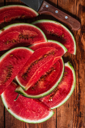 Watermelon slices with knife lying on wooden table. Verticalの写真素材