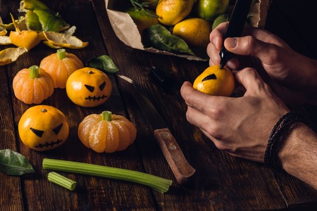 Preparation for Halloween. Young man draws a scary face on tangerinesの写真素材