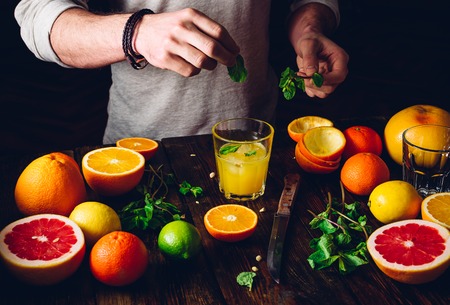 Citrus Cocktail with Ingredients. Guy Puts Mint into Cocktail.