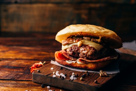 The Casanova Burger on Cutting Board. Cheeseburger with Beef Patty, Wisconsin Swiss Cheese, Ham, Sauteed Mushrooms, Dijon Mustard, Mayonnaise and Potato Roll. Wooden Background and Copy Space.の写真素材
