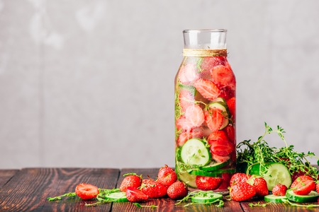 Bottle of Water Flavored with Fresh Strawberry, Sliced Cucumber and Springs of Thyme. Ingredients Scattered on Wooden Table. Copy Space.の写真素材