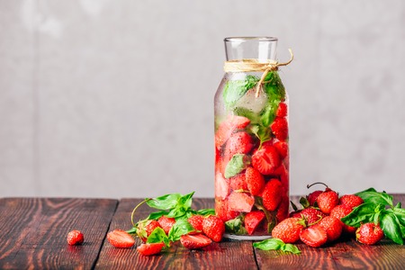 Flavored Water in Bottle with Fresh Strawberry and Basil Leaves. Scattered Ingredients on Wooden Table. Copy Space.の写真素材