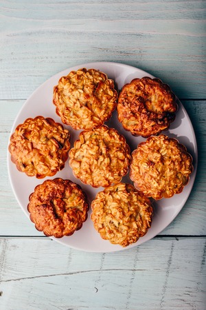 Cooked oatmeal muffins on white plate over light wooden
