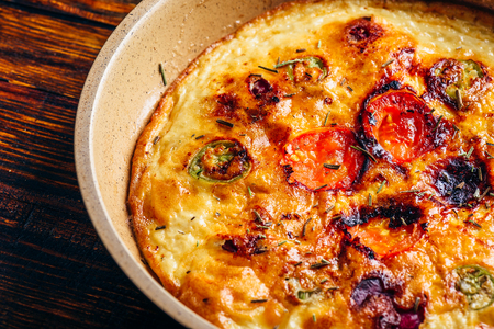 Cooked frittata with chorizo, tomatoes and chili peppers in a frying pan over dark woodenの写真素材