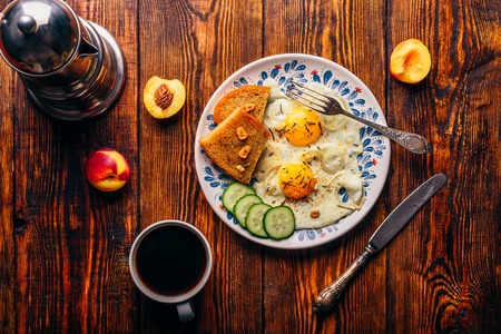 Breakfast toast with fried eggs with vegetables on plate and cup of coffee with fruits over dark woodenの写真素材
