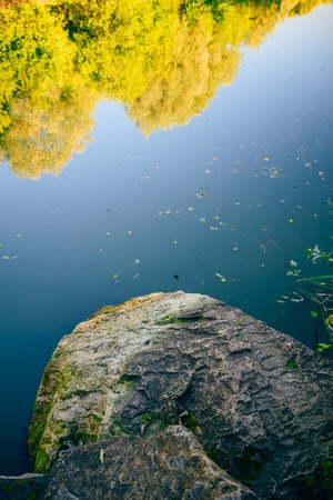 Flooded stone in front of the forest lake with reflection of yellow treesの写真素材