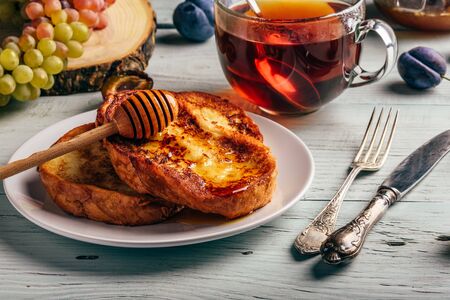 Healthy breakfast concept. French toasts with honey, fruits and tea over white wooden backgroundの写真素材