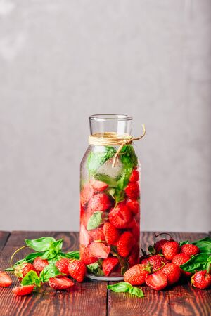 Bottle of Water Infused with Fresh Strawberry and Basil Leaves. Scattered Ingredients on Wooden Table. Vertical Orientation and Copy Space.の写真素材