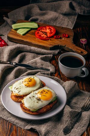 Bruschettas with vegetables and fried eggs on white plate and cup of coffee over grey rough cloth. Healthy food concept.の写真素材