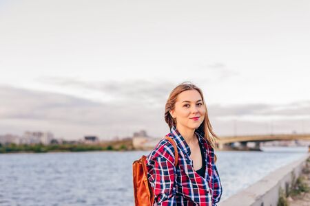 Smiling woman sitting on the riverbank during summer sunsetの写真素材