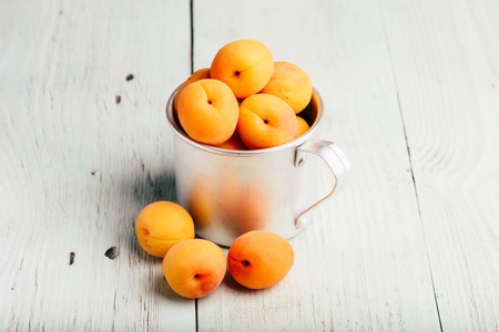 Mellow apricots in metal mug over light wooden surfaceの写真素材