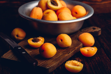 Mellow apricots with knife over old wooden cutting board and metal bowl with fruitsの写真素材