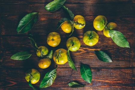 Yellow-green tangerines with leaves over wooden surface. View from above.の写真素材