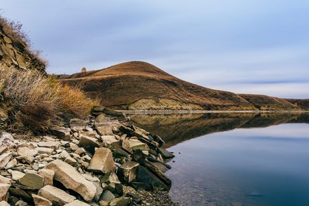 Big boulders on hilly coastline. Overcast sky reflected on lake surface.の写真素材