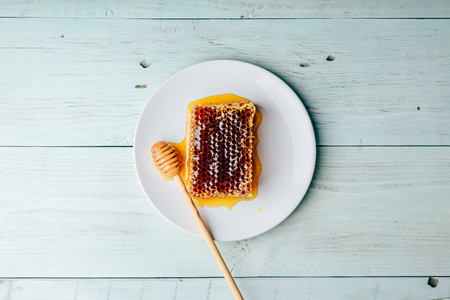 Top view of delicious yummy honeycomb on bright plate with honey dipper over light woodenの写真素材