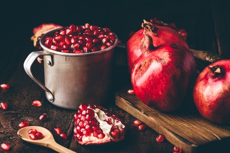 Metal rustic mug full of pomegranate seeds. Whole fruits and pomegranate pieces on dark wooden...