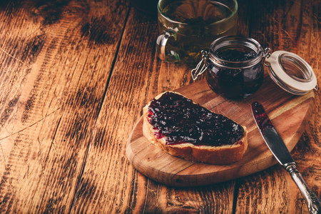 Toast with berry jam on cutting board and cup of green tea in rustic settingの写真素材