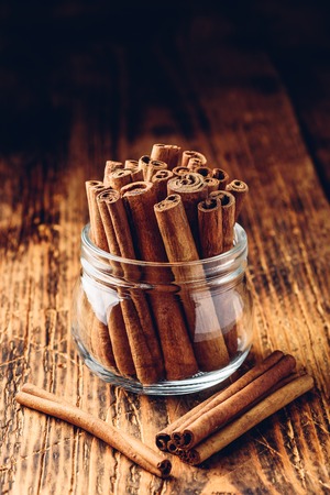 Cinnamon sticks in a glass jar over rustic wooden surfaceの写真素材