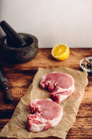 Two pork loin steaks on baking paper with lemon and peppercornの写真素材