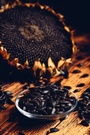 Roasted seeds on the glass saucer and dried sunflower over old wooden surfaceの写真素材