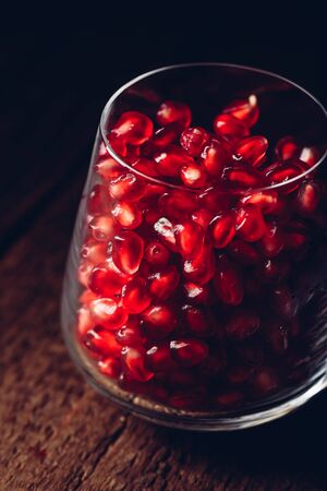 Glass full of red pomegranate seeds on wooden tableの写真素材