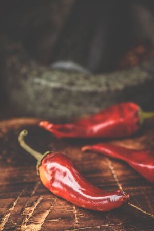Sun dried red chili peppers on wooden surface with mortar and pestleの写真素材