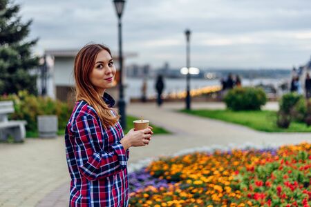 Coffee on the go. Beautiful young woman holding coffee cup and smiling in the parkの写真素材