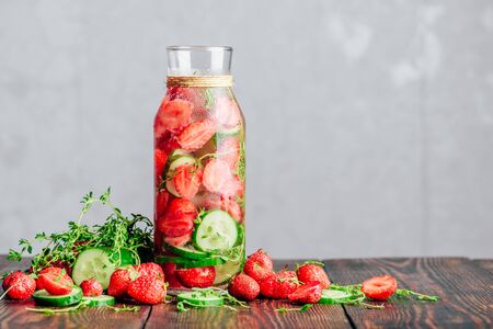 Bottle of Infused Water with Fresh Strawberry, Sliced Cucumber and Springs of Thyme. Ingredients Scattered on Wooden Table. Copy Space.の写真素材