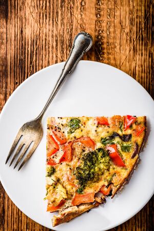Slice of vegetable frittata with broccoli, red bell pepper and red onion on white plate. View from aboveの写真素材