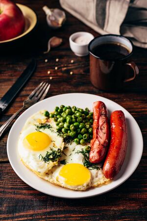 Breakfast with fried eggs, sausages and green peas on white plateの写真素材