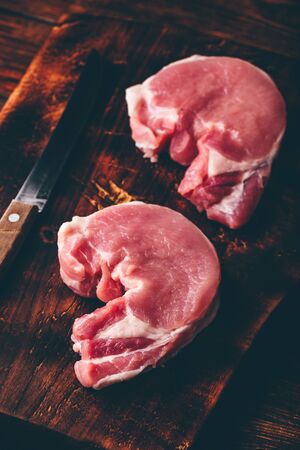 Two pork loin steaks with knife on rustic cutting boardの写真素材