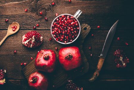 Metal mug full of pomegranate seeds. Whole fruits and pomegranate pieces on rustic wooden table. View from aboveの写真素材