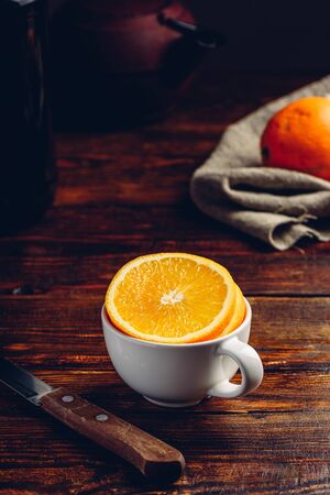 Sliced orange in a white cup on wooden surfaceの写真素材