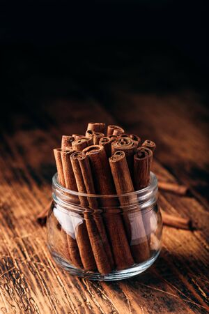 Cinnamon sticks in a glass jar over rustic wooden surfaceの写真素材