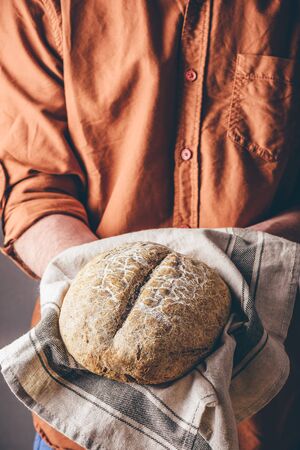 Man holds a loaf of freshly baked rye breadの写真素材
