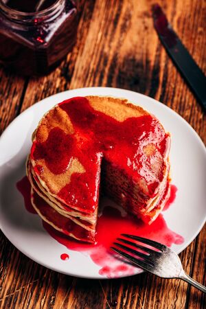 Stack of american pancakes with red berry jam on plate over rustic surfaceの写真素材