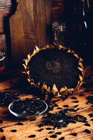 Roasted seeds on the glass saucer and dried sunflower over old wooden surfaceの写真素材