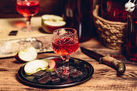 Glass of homemade currant nalivka and chocolate with sliced apple on metal trayの写真素材