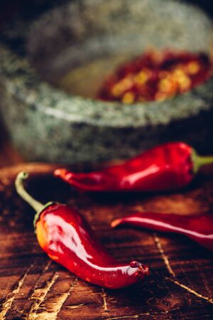 Sun dried red chili peppers on wooden surface with mortar and pestleの写真素材