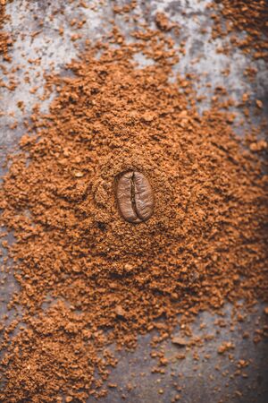 Fresh roasted coffee bean lays on heap of ground coffeeの写真素材