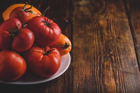 Fresh red and yellow tomatoes on white plate over wooden surfaceの写真素材