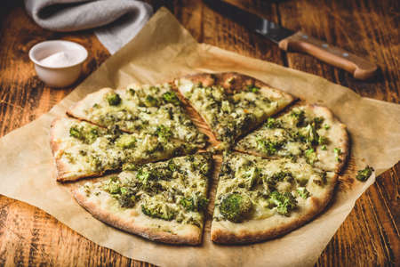 Sliced homemade pizza with broccoli, pesto sauce, spices and cheese on baking paperの写真素材
